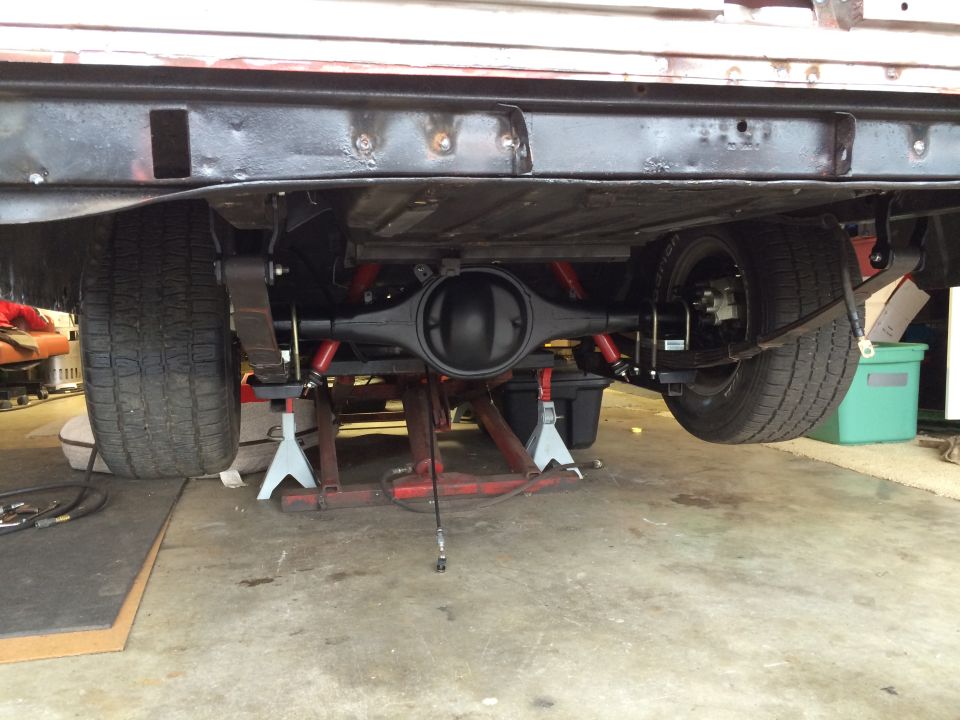 Rear axle assembly and leaf springs on a vehicle supported by jack stands. Red shocks are visible