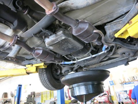 1991 Ford LTD Crown Victoria - An oil drain pan is positioned beneath the transmission and exhaust system of a vehicle undergoing service.