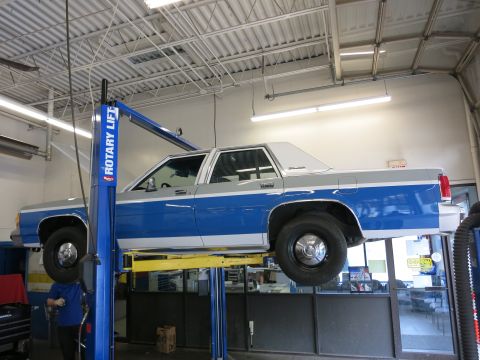 1991 Ford LTD Crown Victoria - A two-tone blue and gray Ford Crown Victoria is raised on a hydraulic lift in an auto repair shop.