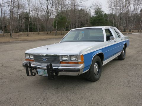 1991 Ford LTD Crown Victoria - A two-tone white and blue Ford Crown Victoria sedan is parked outdoors on a gravel surface with trees in the background.