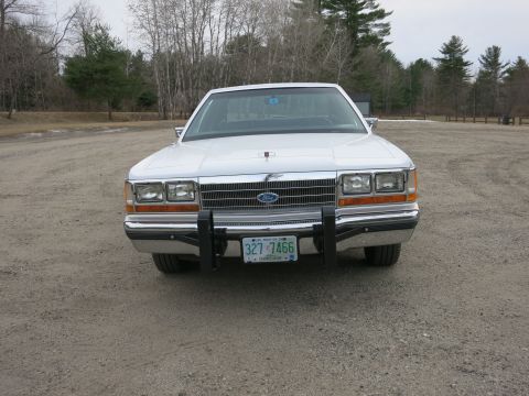 1991 Ford LTD Crown Victoria - This white sedan, likely a 1990 model, is viewed from the front and is equipped with a push bar.