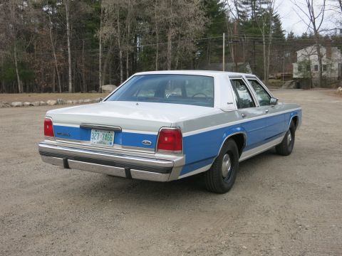 1991 Ford LTD Crown Victoria - This two-tone blue and silver sedan, likely a 1990s Ford Crown Victoria, is seen from the rear.