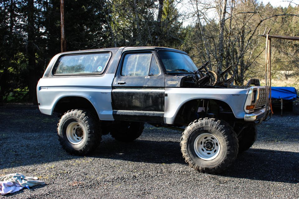 Lifted white and black two-door Bronco-style SUV in mid-build, hood removed, on gravel