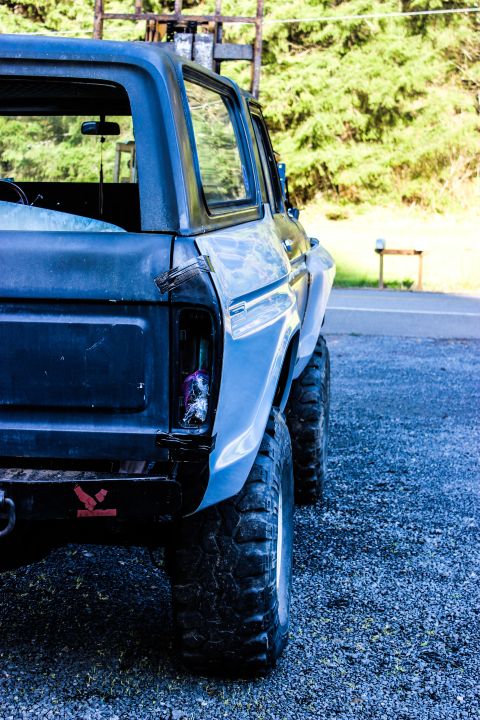 1979 Ford Bronco - The rear of a dark blue 1978 Ford Bronco is visible, showing off-road tires and a damaged taillight.
