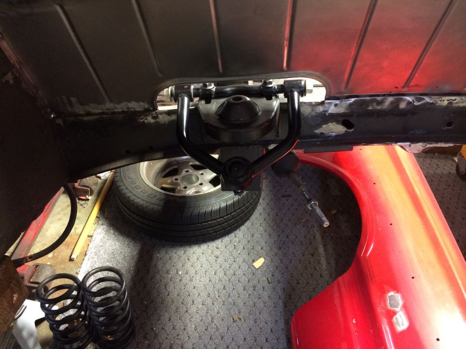 Close-up of a car's upper control arm and suspension components, with a tire and red fender visible