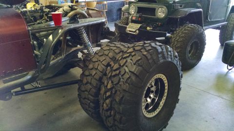 Maroon off-road vehicle chassis with exposed engine and large dual tires, next to a green vehicle