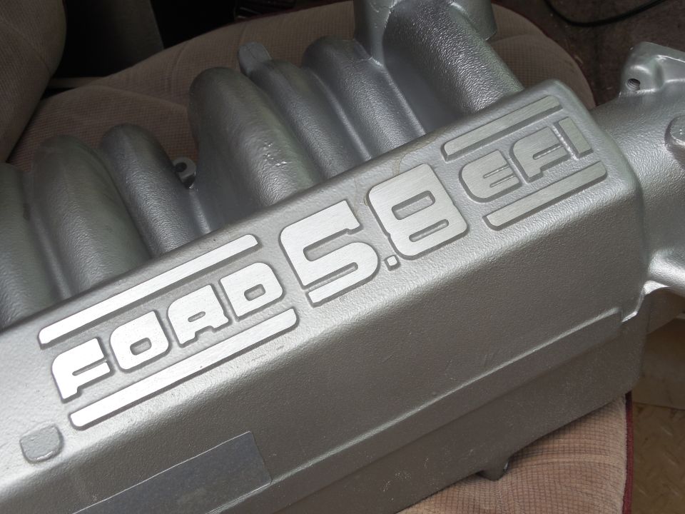 Silver-painted Ford 5.8 EFI upper intake manifold resting on a cloth seat