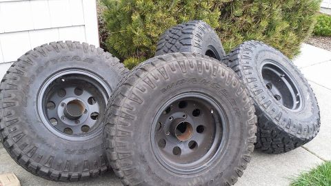 1978 Ford Bronco - A collection of four tires and rims are displayed outdoors, with a building and greenery in the background.