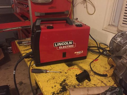 1994 Ford Bronco - A red Lincoln Electric welder sits on a cluttered yellow workbench next to a screwdriver and other tools.