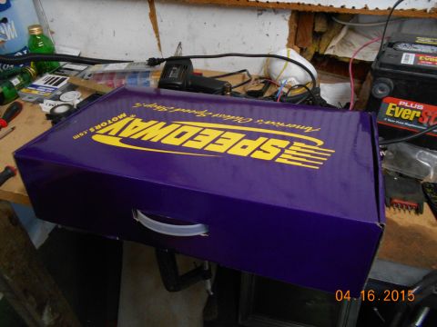 1978 Ford Bronco - A purple box from Speedway Motors sits on a cluttered workbench next to a car battery and various tools.