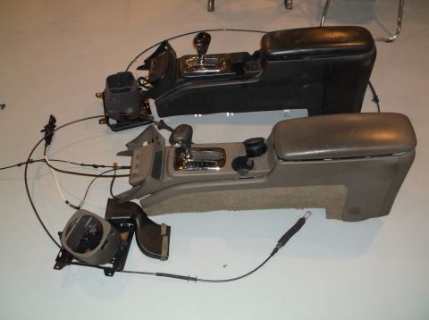 1999 Mercury Grand Marquis - Two center consoles, one black and one tan, are shown disassembled with their gear shifters and armrests removed from a vehicle.