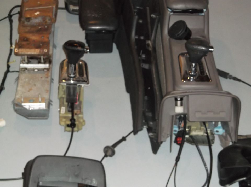 Car interior parts, including two gear shifters and console pieces, laid out on a surface