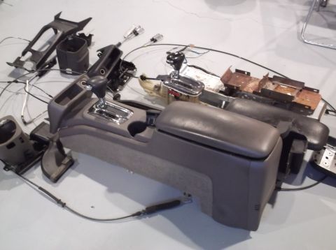 1999 Mercury Grand Marquis - Disassembled car interior console components, including the gear shifter and armrest, laid out on a floor.