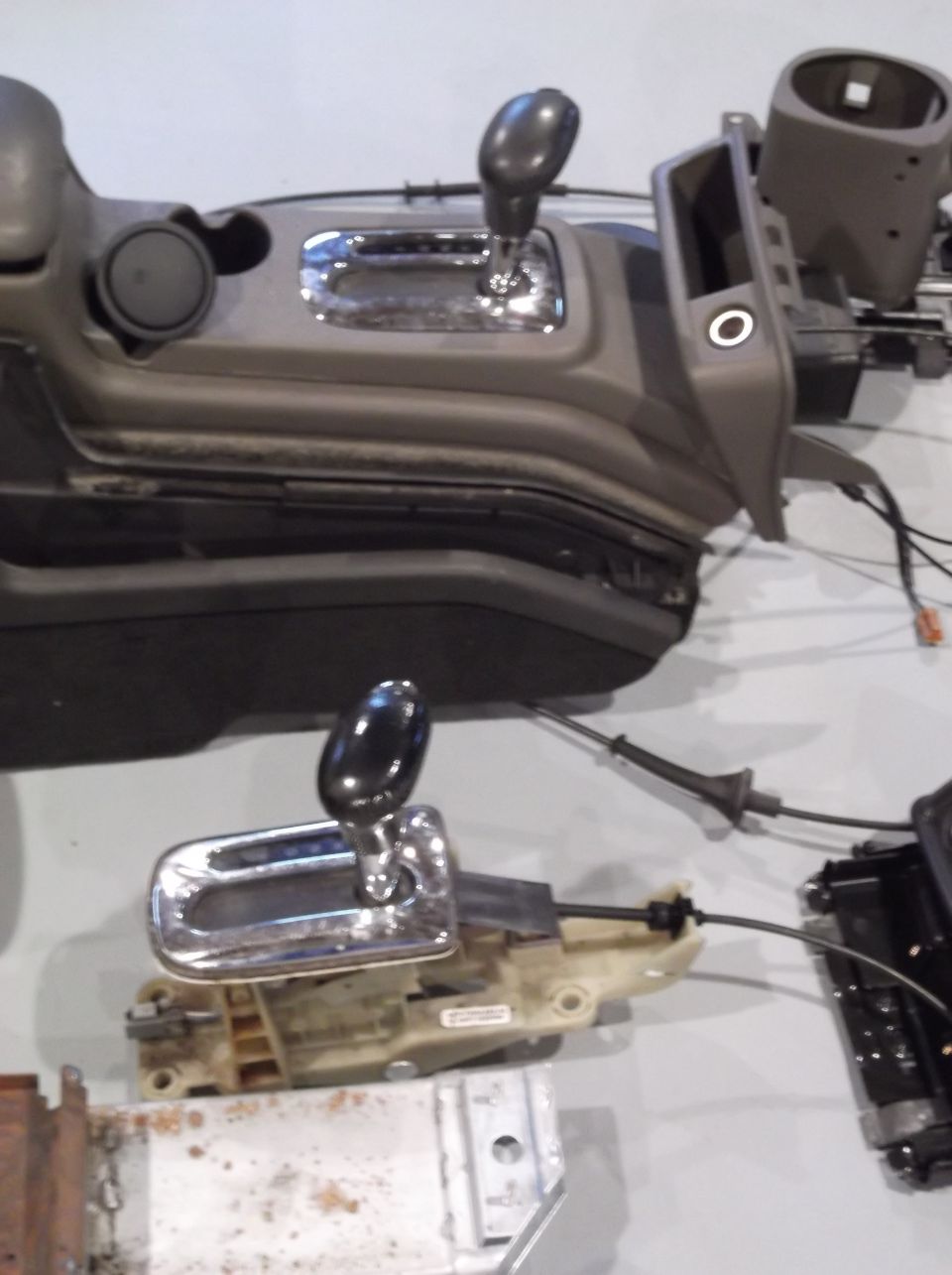 Two car center consoles with gear shifters and wiring, one above the other