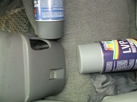 1999 Mercury Grand Marquis - Two cans of spray paint are placed on the carpeted floor of a vehicle, next to a gray plastic trim piece.