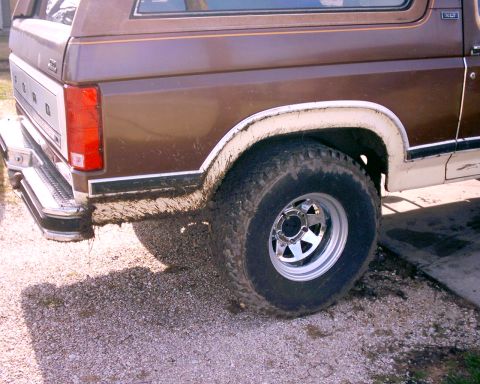 1980 Ford Bronco - The rear of a brown 1980 Ford Bronco shows its quarter panel and tire, caked with mud from off-road use.