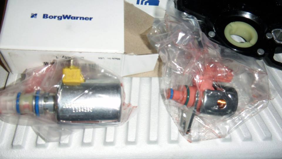 Two new BorgWarner transmission solenoids in plastic packaging, one silver with a yellow connector, the other red and black