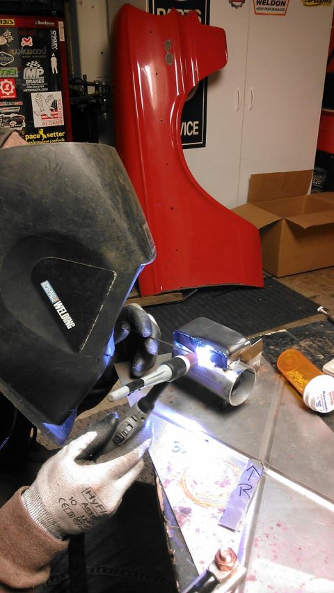1964 Ford Fairlane - A red car fender with a "50" badge is visible while a person welds metal parts in a workshop.