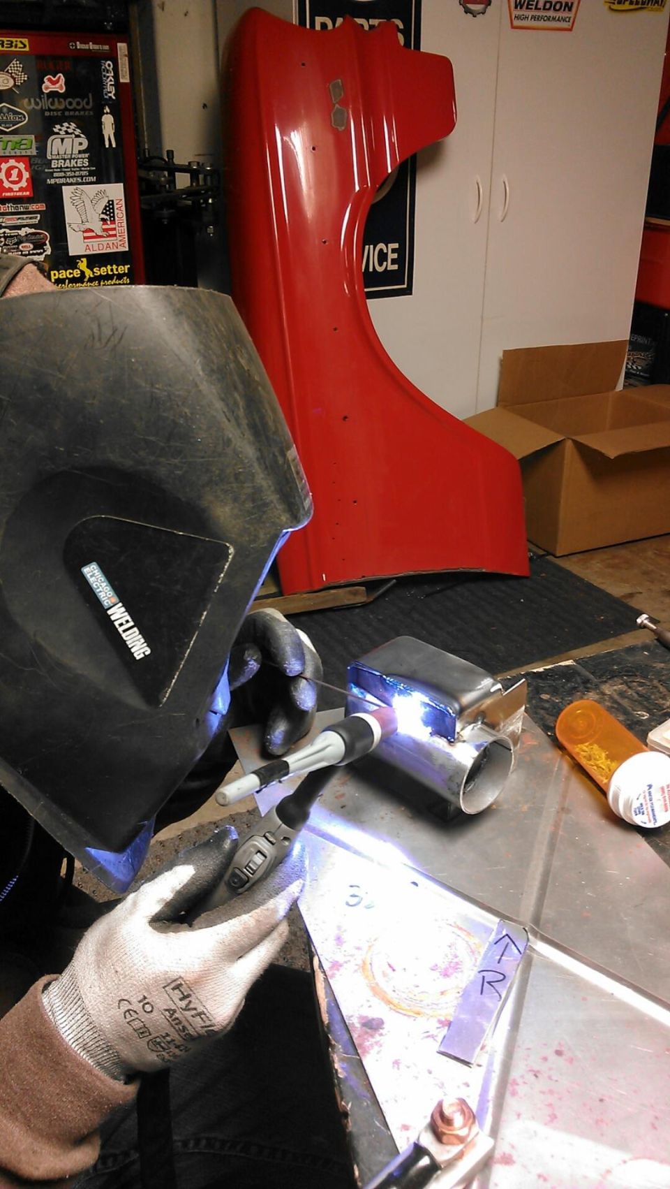 Red car fender with a "50" badge, viewed from the side, with a person welding in the foreground