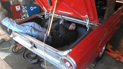 1964 Ford Fairlane - A person works inside the trunk of a red 1964 Ford Fairlane, with the trunk lid open and tools visible.