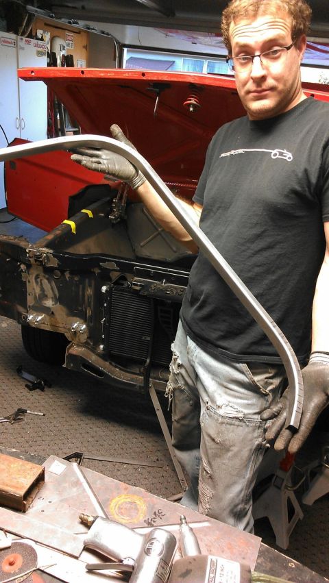 1964 Ford Fairlane - A man holds a piece of trim in front of the engine bay of a 1964 Ford Fairlane undergoing restoration.