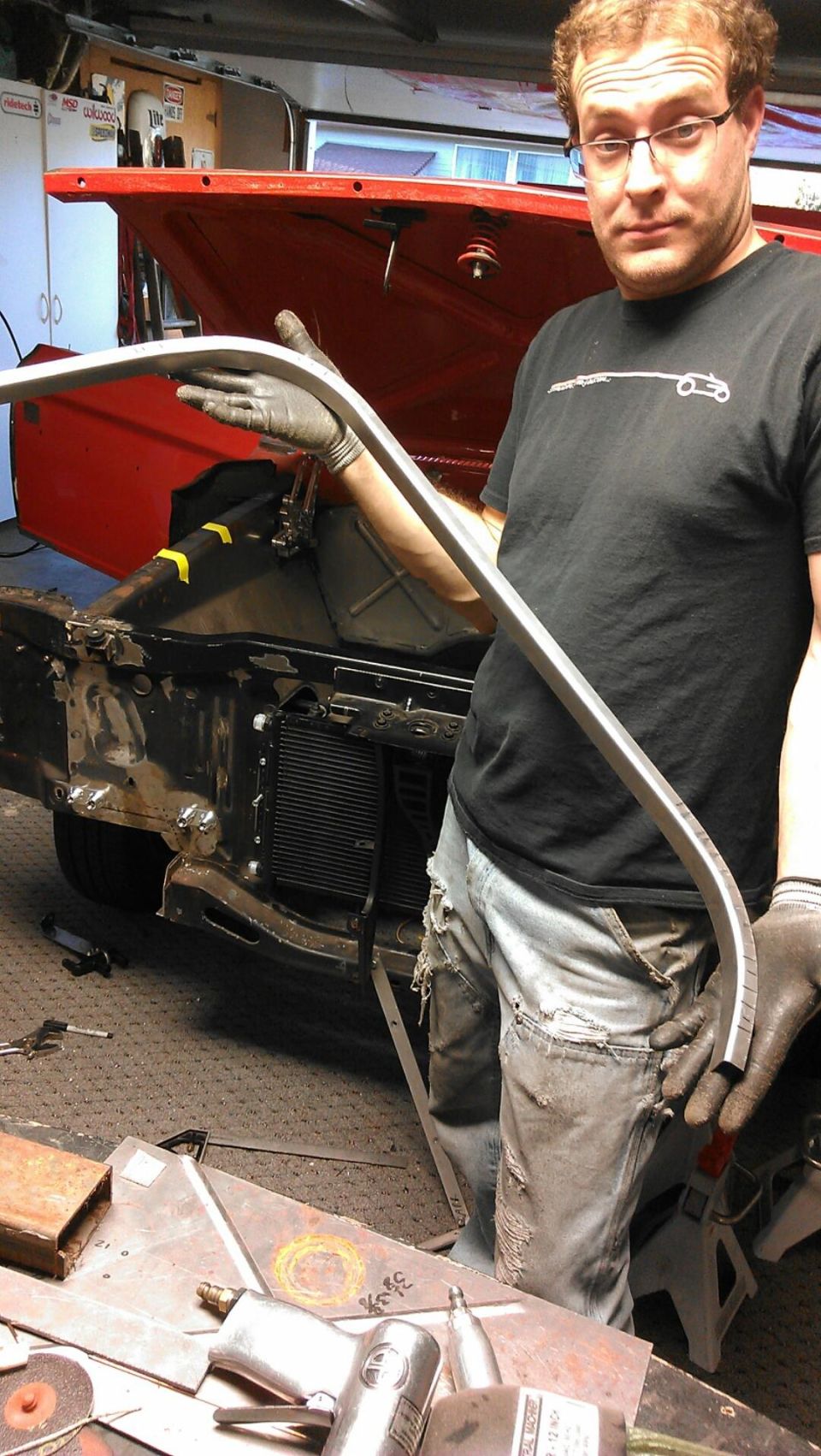 Man holding curved metal trim in front of 1964 Ford Fairlane engine bay