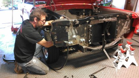 1964 Ford Fairlane - Mechanic works on the front end of a 1964 Ford Fairlane, exposing the radiator and engine bay for repair.