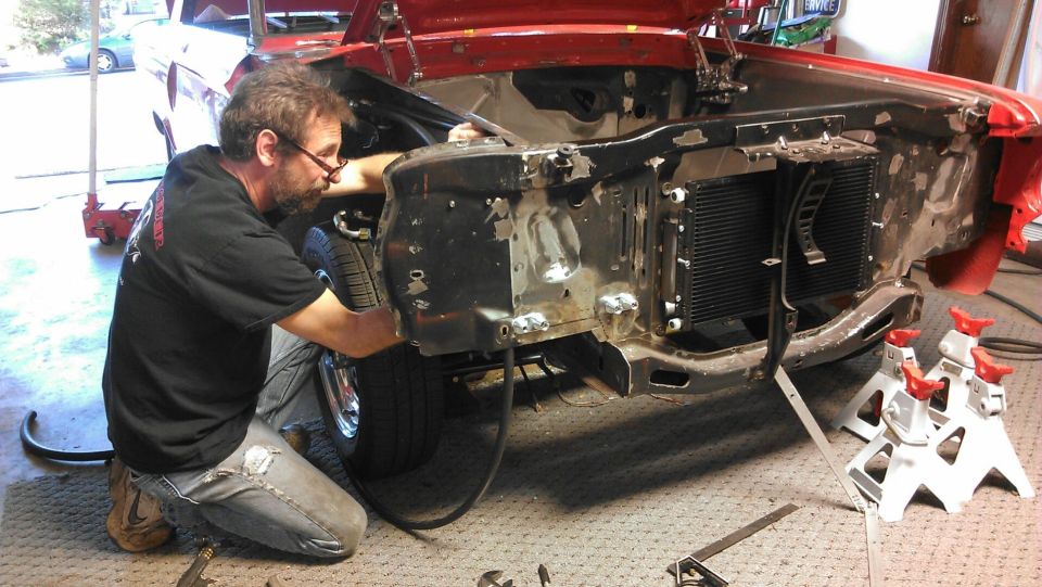 Man working on the front end of a red 1964 Ford Fairlane, with the hood open and radiator exposed