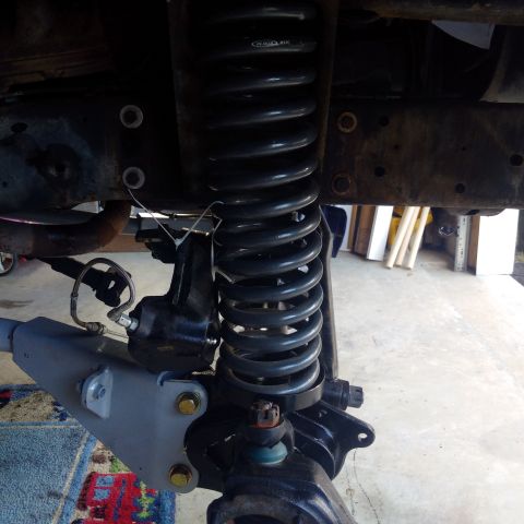1978 Ford Bronco - Close-up view of a vehicle's front suspension system, focusing on the coil spring and shock absorber components.