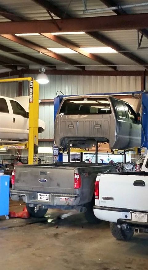 1986 Ford Bronco - A truck cab is suspended in a garage, undergoing repairs with other vehicles nearby.