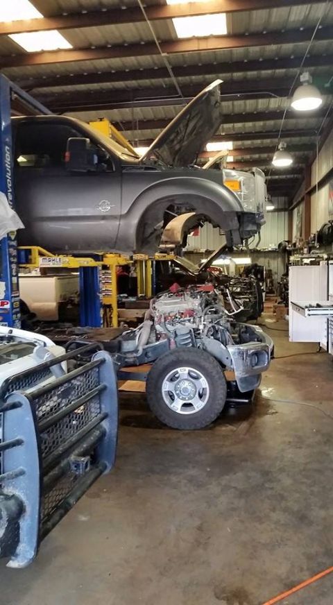 1986 Ford Bronco - A truck's cab is raised on a lift while its chassis and engine are exposed in a workshop.