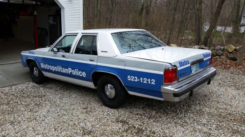 1991 Ford LTD Crown Victoria - This 1991 Ford Crown Victoria LTD police car is seen from the rear 3/4 angle, displaying 'Metropolitan Police' and a phone number.