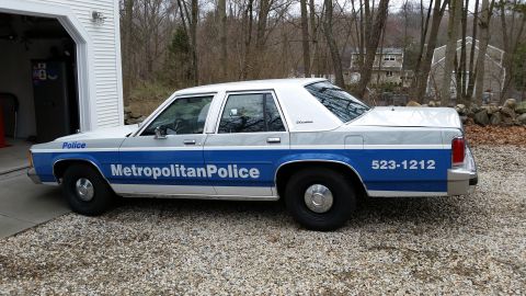 1991 Ford LTD Crown Victoria - A police car with a two-tone paint scheme is parked in front of a garage.