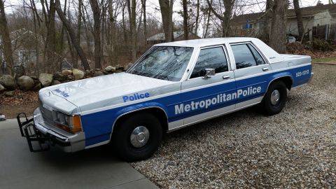 1991 Ford LTD Crown Victoria - A 1991 Ford Crown Victoria LTD police car is shown from a three-quarter front angle, parked on a gravel surface.