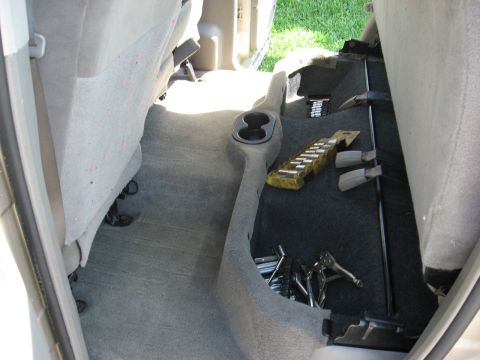 1994 Ford Bronco - The rear interior of a vehicle shows a cup holder, tools, and carpeted floor.
