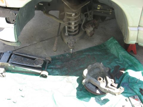 1994 Ford Bronco - A disassembled front suspension component rests on a green tarp next to a floor jack, indicating repair work.