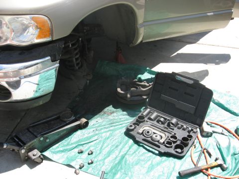 1994 Ford Bronco - Truck front end disassembled for repair, with a tool kit and jack visible on a tarp.