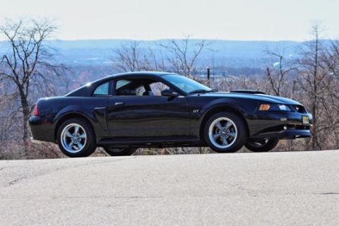 2002 Ford Mustang - Side profile of a black Ford Mustang GT with aftermarket wheels.