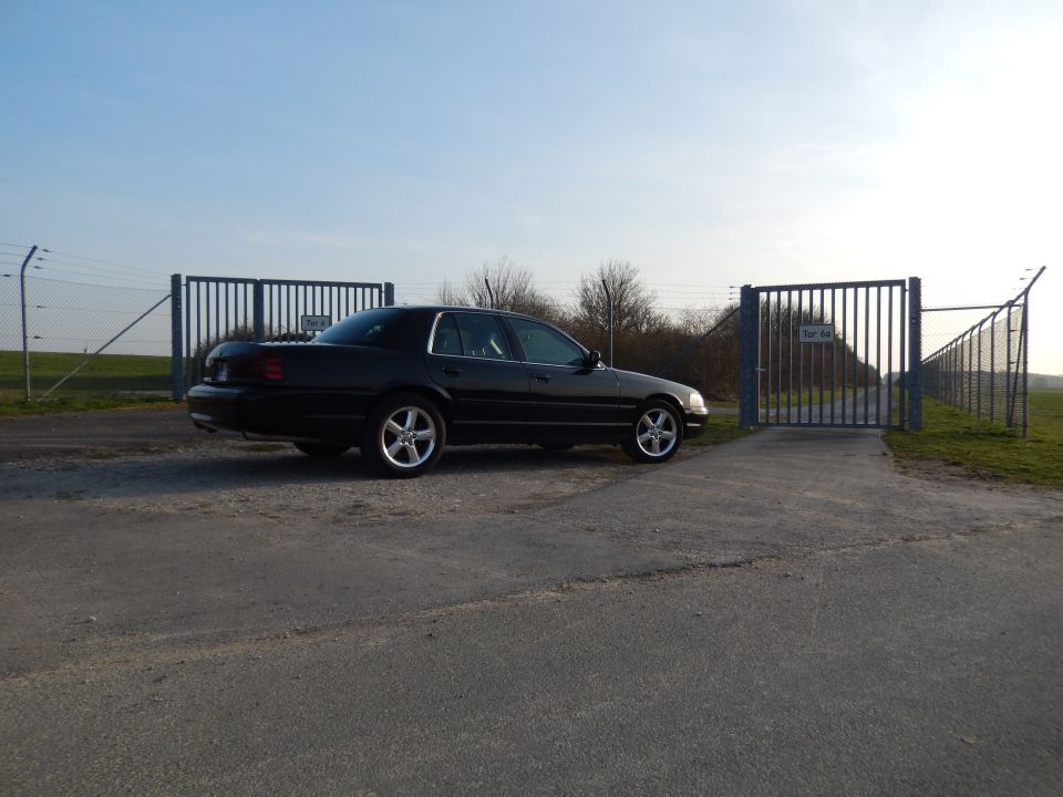 Black sedan parked on a gravel lot in front of a closed gate