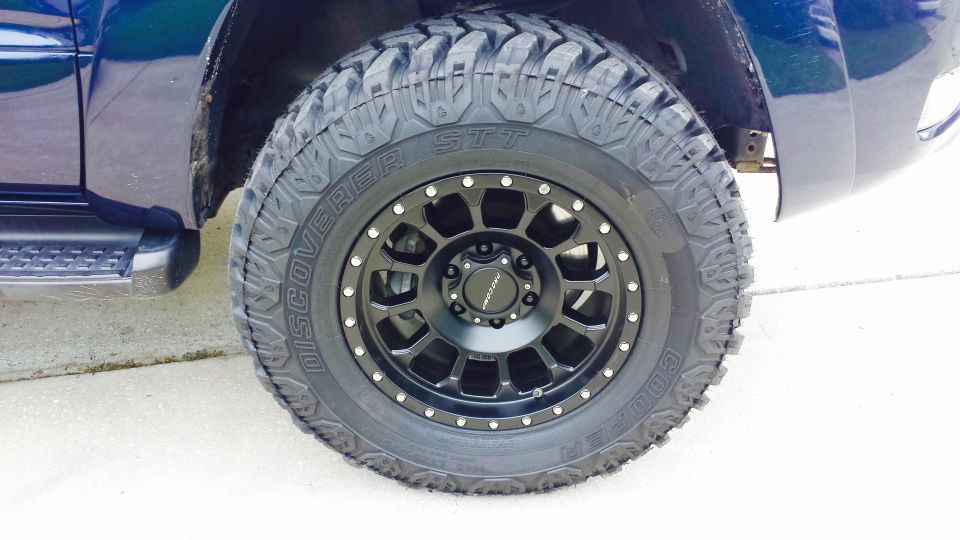 Close-up of a black aftermarket wheel with Discoverer STT tires on a blue SUV