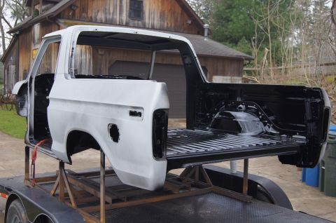 1979 Ford Bronco - White Ford Bronco body on a trailer, undergoing restoration with the bed painted black.
