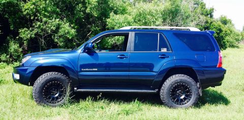 2005 Toyota 4Runner - This blue Toyota 4Runner is shown from the side, aftermarket wheels and tires against a backdrop of greenery.