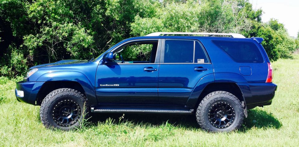 Blue Toyota 4Runner parked in grass with trees behind it. It has black aftermarket wheels and tires