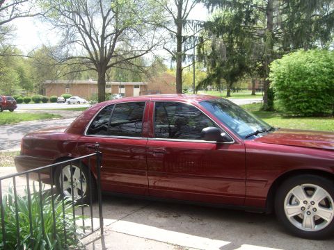 2004 Ford Crown Victoria - A maroon 2004 Ford Crown Victoria is parked on a concrete driveway with trees and a building in the background.
