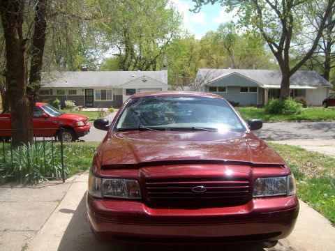 2004 Ford Crown Victoria - A red Ford Crown Victoria is parked in a driveway with a red pickup truck in the background.
