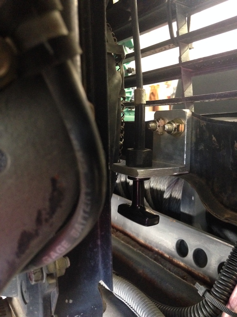 Close-up of an aftermarket hood latch mechanism mounted to a vehicle's grille support