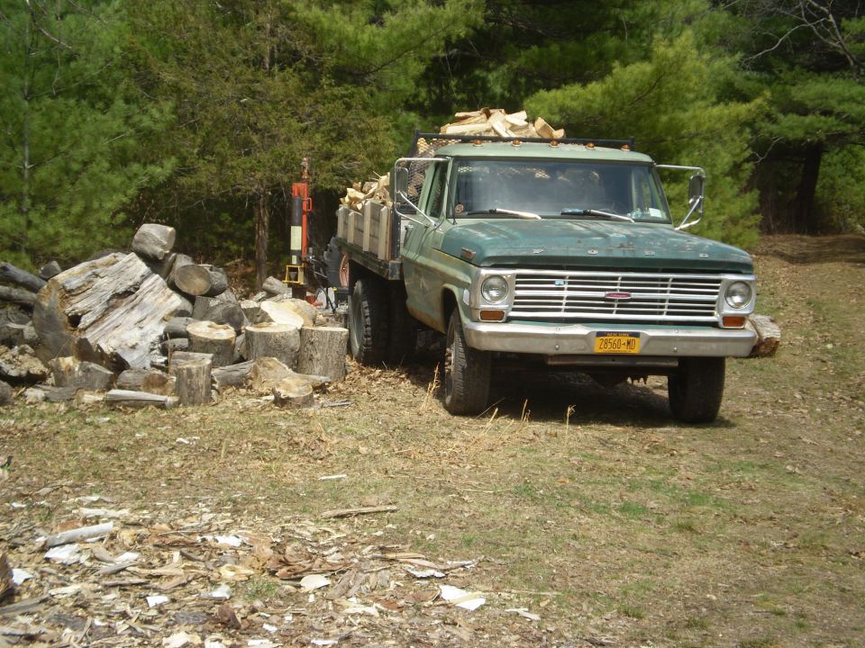 Green 1967 Ford F-series truck loaded with firewood, parked next to a woodpile