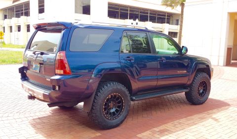 2005 Toyota 4Runner - This blue 2005 Toyota 4Runner is equipped with off-road tires and a rear spoiler, seen parked on a brick surface.