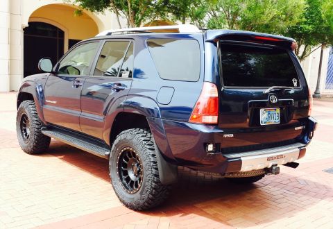 2005 Toyota 4Runner - A dark blue SUV with off-road tires is parked on a brick surface near a building.
