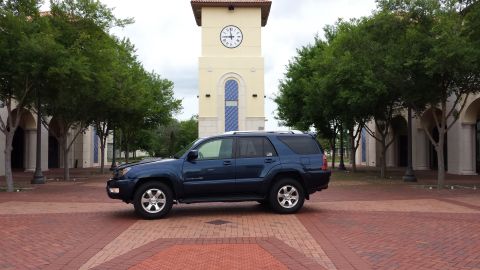 2005 Toyota 4Runner - A blue 2005 Toyota 4Runner is parked on brick paving in front of a clock tower and trees.